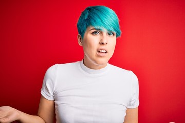 Young beautiful woman with blue fashion hair wearing casual t-shirt over red background clueless...