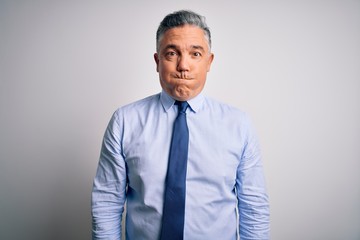 Middle age handsome grey-haired business man wearing elegant shirt and tie puffing cheeks with funny face. Mouth inflated with air, crazy expression.