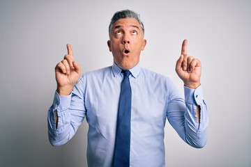 Middle age handsome grey-haired business man wearing elegant shirt and tie amazed and surprised looking up and pointing with fingers and raised arms.