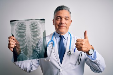 Middle age handsome grey-haired doctor man holding chest xray over white background happy with big...