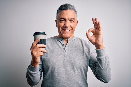 Middle age handsome grey-haired man drinking cup of coffee over isolated white background doing ok sign with fingers, excellent symbol
