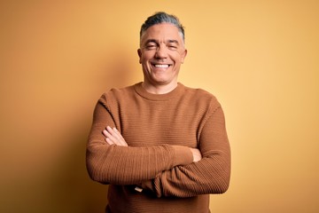 Middle age handsome grey-haired man wearing casual sweater over yellow background happy face smiling with crossed arms looking at the camera. Positive person.