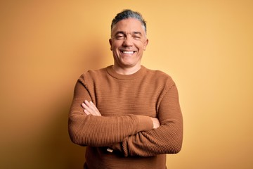 Middle age handsome grey-haired man wearing casual sweater over yellow background happy face smiling with crossed arms looking at the camera. Positive person. - Powered by Adobe