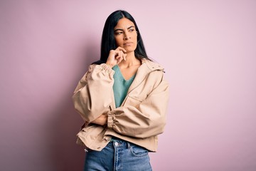 Young beautiful hispanic fashion woman wearing winter jacket and sweater over pink background with hand on chin thinking about question, pensive expression. Smiling with thoughtful face. Doubt