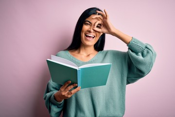 Young beautiful hispanic student woman reading a book over pink isolated background with happy face smiling doing ok sign with hand on eye looking through fingers