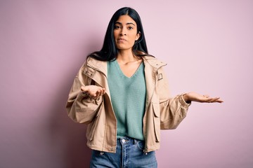 Young beautiful hispanic fashion woman wearing winter jacket and sweater over pink background...
