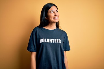 Young beautiful hispanic woman wearing volunteer t-shirt as social charity moral smiling looking to...
