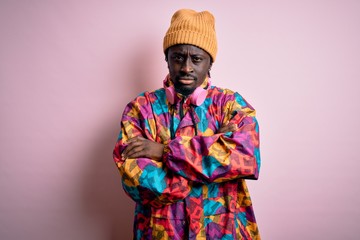 Young handsome african american man wearing colorful coat and cap over pink background skeptic and...