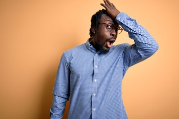 Young handsome african american man wearing shirt and glasses over yellow background surprised with...