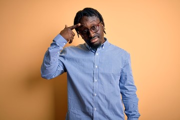 Young handsome african american man wearing shirt and glasses over yellow background pointing...