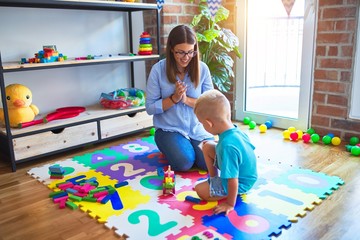 Young caucasian child playing at playschool with teacher. Mother and son playing with wooden pieces train at playroom