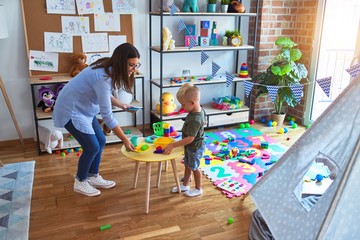Young caucasian child playing at playschool with teacher. Mother and son at playroom cooking at toy...