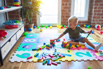 Young caucasian kid playing at kindergarten with toys. Preschooler boy happy at playroom.