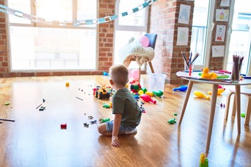 Young caucasian kid playing at kindergarten with toys. Preschooler boy happy at playroom.