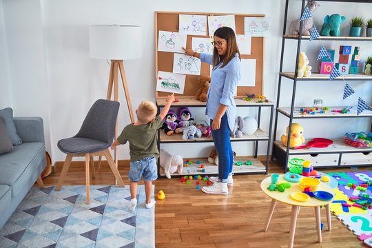 Young caucasian child playing at playschool with teacher. Mother and son at playroom around toys.