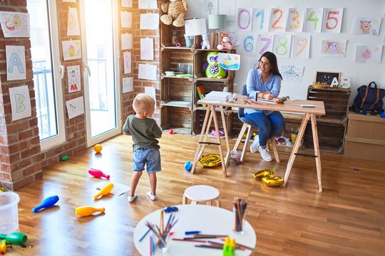 Young caucasian child playing at playschool with teacher. Young woman sitting on the desk of the classroom