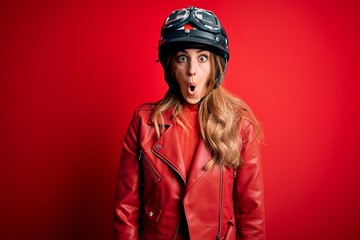 Young beautiful brunette motrocyclist woman wearing moto helmet over red background afraid and shocked with surprise expression, fear and excited face.