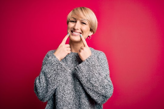 Young blonde woman with modern short hair wearing casual sweater over pink background Smiling with open mouth, fingers pointing and forcing cheerful smile