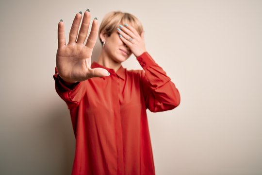 Young beautiful business blonde woman with short hair standing over isolated background covering eyes with hands and doing stop gesture with sad and fear expression. Embarrassed and negative concept.