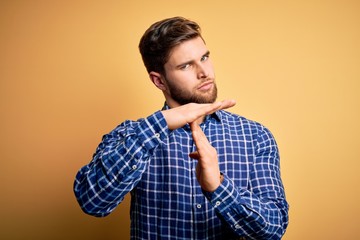 Young blond businessman with beard and blue eyes wearing shirt over yellow background Doing time...