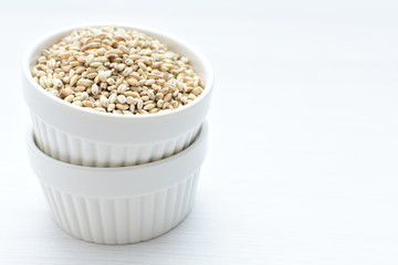 Raw barley grains, released in containers on white wooden background