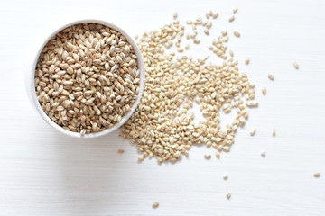 Raw barley grains, released in containers on white wooden background
