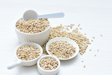 Raw barley grains, released in containers on white wooden background