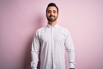 Young handsome man with beard wearing casual shirt standing over pink background with a happy and cool smile on face. Lucky person.