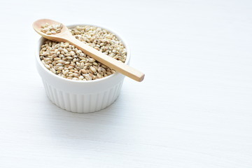 Raw barley grains, released in containers on white wooden background