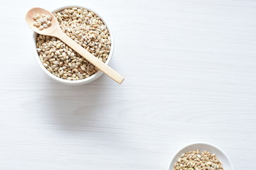 Raw barley grains, released in containers on white wooden background