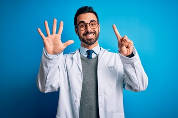 Young handsome doctor man with beard wearing coat and glasses over blue background showing and pointing up with fingers number six while smiling confident and happy.