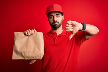 Young handsome delivery man with beard wearing cap holding takeaway paper bag with food with angry face, negative sign showing dislike with thumbs down, rejection concept