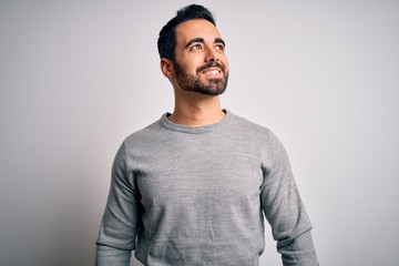 Young handsome man with beard wearing casual sweater standing over white background looking away to side with smile on face, natural expression. Laughing confident.