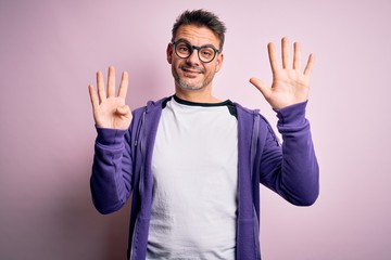 Young handsome man wearing purple sweatshirt and glasses standing over pink background showing and...
