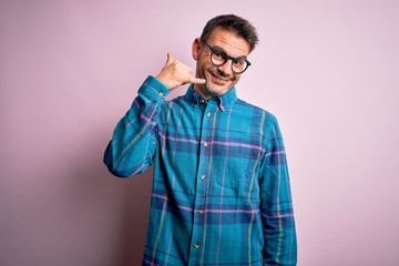 Fototapeta premium Young handsome man wearing casual shirt and glasses standing over isolated pink background smiling doing phone gesture with hand and fingers like talking on the telephone. Communicating concepts.