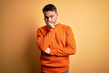 Young handsome man wearing orange casual sweater standing over isolated yellow background thinking...
