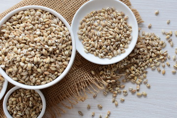 Raw barley grains, released in containers on white wooden background
