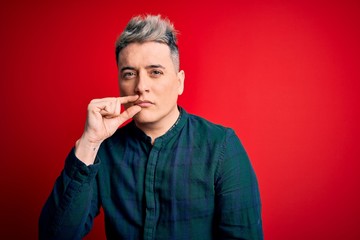 Young handsome modern man wearing elegant green shirt over red isolated background mouth and lips shut as zip with fingers. Secret and silent, taboo talking