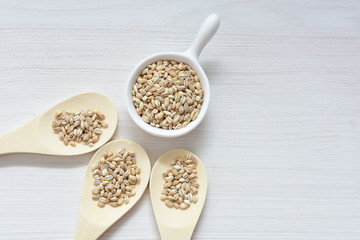 Raw barley grains, released in containers on white wooden background