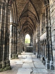 Long arch hallway with stone columns of ancient Holyrood Abbey and Palace Castle in Edinburgh. Home of King James and Mary. Scotland, Great Britain, United Kingdom, Europe.  The Highlander Life.