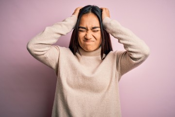 Young beautiful asian woman wearing casual turtleneck sweater over pink background suffering from headache desperate and stressed because pain and migraine. Hands on head.