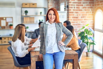 Group of business workers working together. Young beautiful businesswoman standing smiling happy looking at the camera at the office