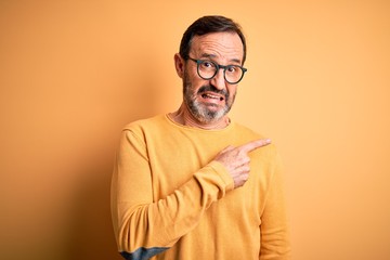 Obraz premium Middle age hoary man wearing casual sweater and glasses over isolated yellow background Pointing aside worried and nervous with forefinger, concerned and surprised expression