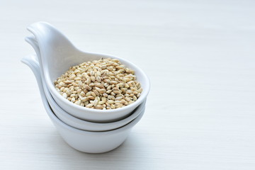 Raw barley grains, released in containers on white wooden background