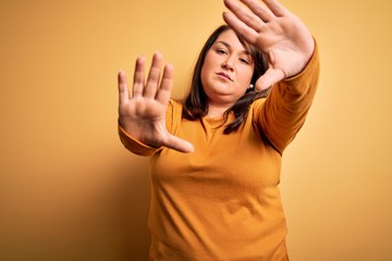 Beautiful brunette plus size woman wearing casual sweater over isolated yellow background doing frame using hands palms and fingers, camera perspective