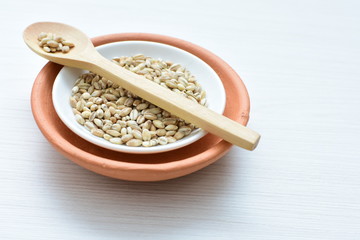 Raw barley grains, released in containers on white wooden background