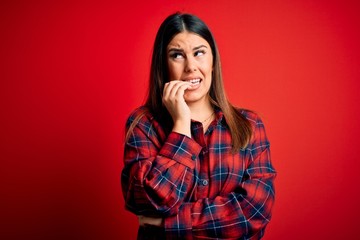 Young beautiful woman wearing casual shirt over red background looking stressed and nervous with hands on mouth biting nails. Anxiety problem.