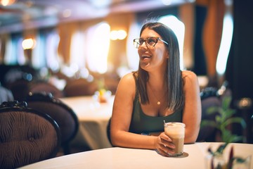 Young beautiful woman smiling happy and confident. Sitting with smile on face holding glass of coffee at restaurant