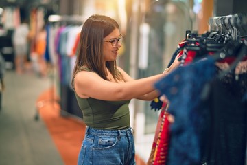 Young beautiful woman smiling happy and confident. Standing with smile on face looking clothes at store