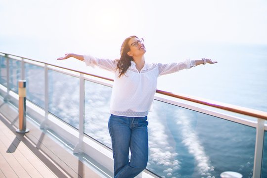 Young beautiful woman on vacation smiling happy and confident. Standing on a deck of ship with smile on face and open arms doing a cruise